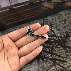 Detail of hand holding a black enamel matchstick brooch with silver edges and flame design