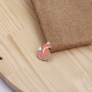 Detail of cute enamel fox brooch with orange and white finish on wood texture