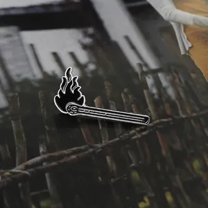 Detailed close-up of a black enamel matchstick pin featuring a burning flame design
