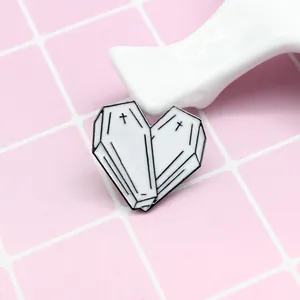 Detailed close-up of heart enamel pin made of two white coffins with black crosses