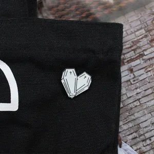 Black and white enamel heart coffin brooch with cross pins on black canvas background