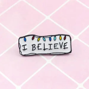 Broche en émail avec texte 'I BELIEVE' et ampoules colorées sur fond quadrillé
