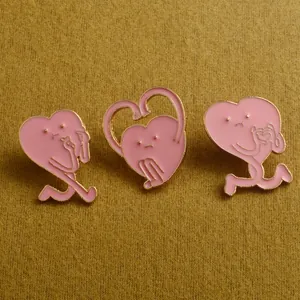 Vue détaillée de trois broches coeur en émail rose avec différents gestes sur tissu jaune