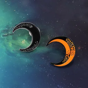 Detail of crescent moon enamel pins in black starry texture and orange moon surface