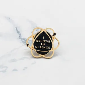Detail of I BELIEVE IN SCIENCE enamel pin with gold atomic orbits on marble