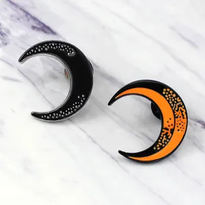 Close-up of black and orange crescent moon enamel pins on white marble surface