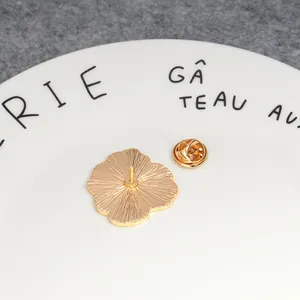 Broche fleur en émail doré avec fermoir papillon présentée sur une assiette en céramique