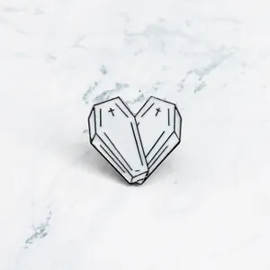 Macro view of white enamel coffin heart brooch with black crosses on marble background