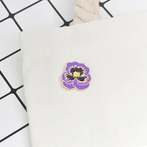 Détail d'une broche en émail pensée violette épinglée sur un sac en toile blanche