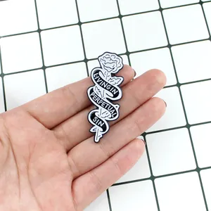 Detalle de pin de rosa esmaltada en mano con texto en cinta de estilo gótico