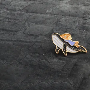 Détail d'un pin's baleine en émail avec une fille sur un fond de pierre texturé gris