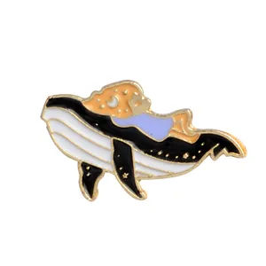 Détail du pin's émaillé en forme de baleine avec finitions dorées sur fond blanc