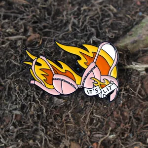 Enamel bikini pin badge with flames and IT'S LIT slogan on rustic wood background