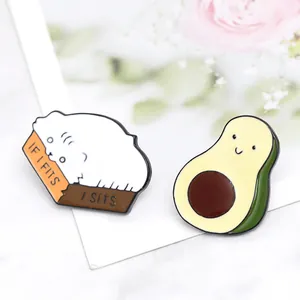 Detailed close-up of cartoon enamel pins featuring a white cat in a box and a cute avocado