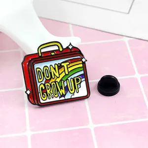 Cartoon red suitcase enamel pin with 'DON'T GROW UP' rainbow design and rubber back
