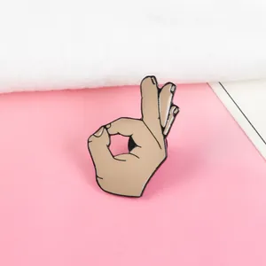 Detail view of a skin-toned OK gesture enamel pin with black outlines and secure back