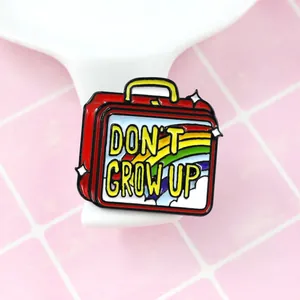 Cartoon enamel pin featuring a red vintage lunchbox with rainbow and Don't Grow Up text