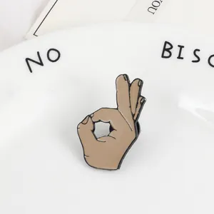 Detailed view of an OK gesture enamel pin with a rose coffee finish on a white plate