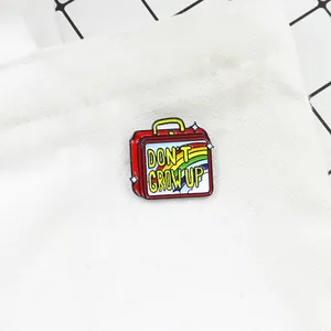 Detail of a red enamel suitcase brooch with Don't Grow Up slogan on a white canvas bag
