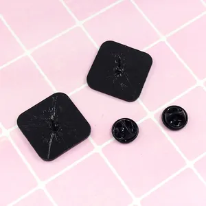 Rear view of two black square metal badges with butterfly clutches on pink grid background