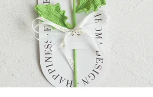 Detail of hand-knitted green flower with Love is Eternal ribbon on white packaging