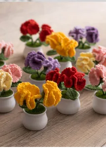 Top-down view of colorful handmade crochet carnation potted plants on a wooden table