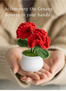 Close-up of handmade crochet red carnations in a small white pot held in hands