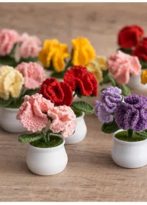 Detailed close-up of handmade crochet carnations in a mini pot on a warm wooden desk