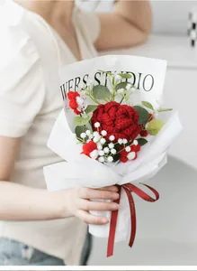 Detail of hand-crocheted red carnation bouquet featuring intricate knitting and gift ribbon