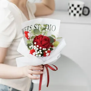 Handgehäkelter roter Rosenstrauß mit grünen Blättern in weißer Geschenkverpackung