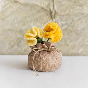Détail de fleurs d'œillets jaunes au crochet dans un pot en toile de jute rustique