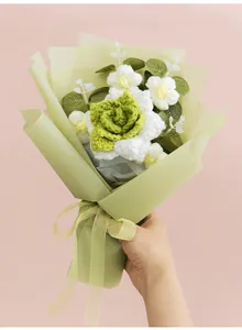 Handheld view of handmade crochet rose and daisy bouquet with green wrapping paper