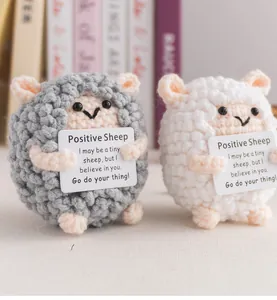 Close-up of handmade crochet sheep dolls with inspirational cards on wooden desk