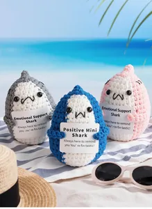 Three handmade crochet shark dolls holding cards in a sunny beach vacation setting