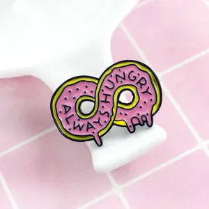 Macro shot of an infinity donut enamel pin with pink glaze and Always Hungry text details