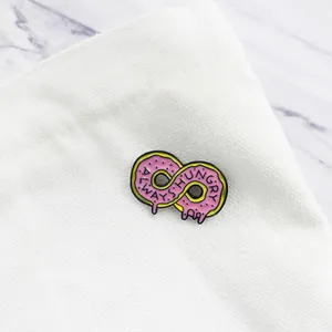 Detail of pink donut infinity symbol enamel pin with Always Hungry text on white canvas