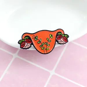 Macro detail of female uterus enamel brooch featuring red roses on orange metal background