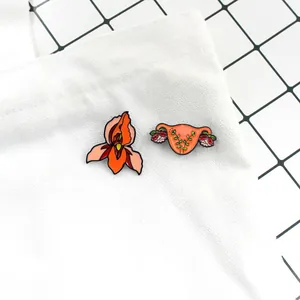 Enamel pins detail showing reproductive system and orange flower on white canvas bag