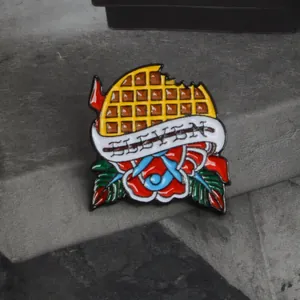 Enamel pin with yellow waffle, red rose, and Eleven text on dark stone background