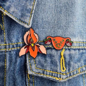 Artistic uterus and orange flower enamel pin set styled on a blue denim jacket