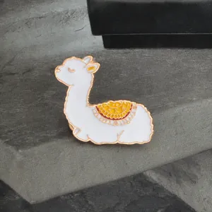 Charmante broche lama en émail blanc avec selle colorée sur un fond gris neutre