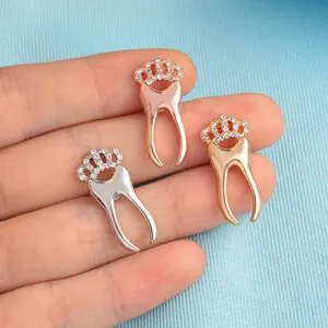 Three crown-topped tooth brooches with rhinestones in gold, silver, and rose gold finishes