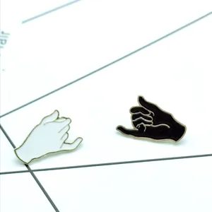 Detail of black and white pinky promise enamel pins with gold trim on a jacket card
