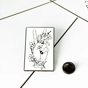 Minimalist black and white enamel pin featuring hand-drawn hand gesture and floral design