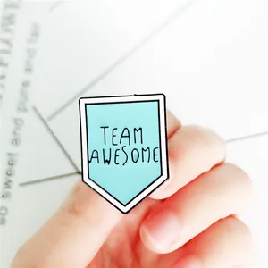 Dettaglio ravvicinato della spilla smaltata Team Awesome tenuta in mano per mostrarne le dimensioni