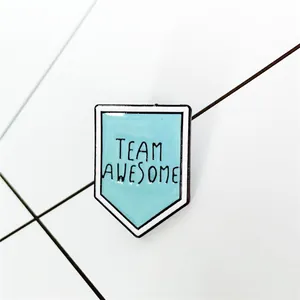 Dettaglio della spilla in smalto Team Awesome con design a scudo e freccia blu