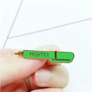Macro shot of green and gold fountain pen enamel pin with MIGHTIER engraved text