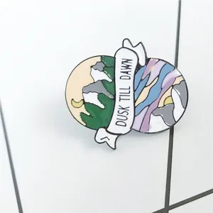 Detailed enamel pin badge featuring moon and mountain with Dusk Till Dawn banner design