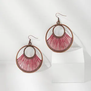 Close-up of geometric round earrings with deep pink woven thread and brass finish