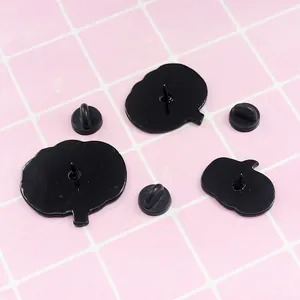 Black enamel pumpkin pin badges in three sizes with secure butterfly backings on pink grid